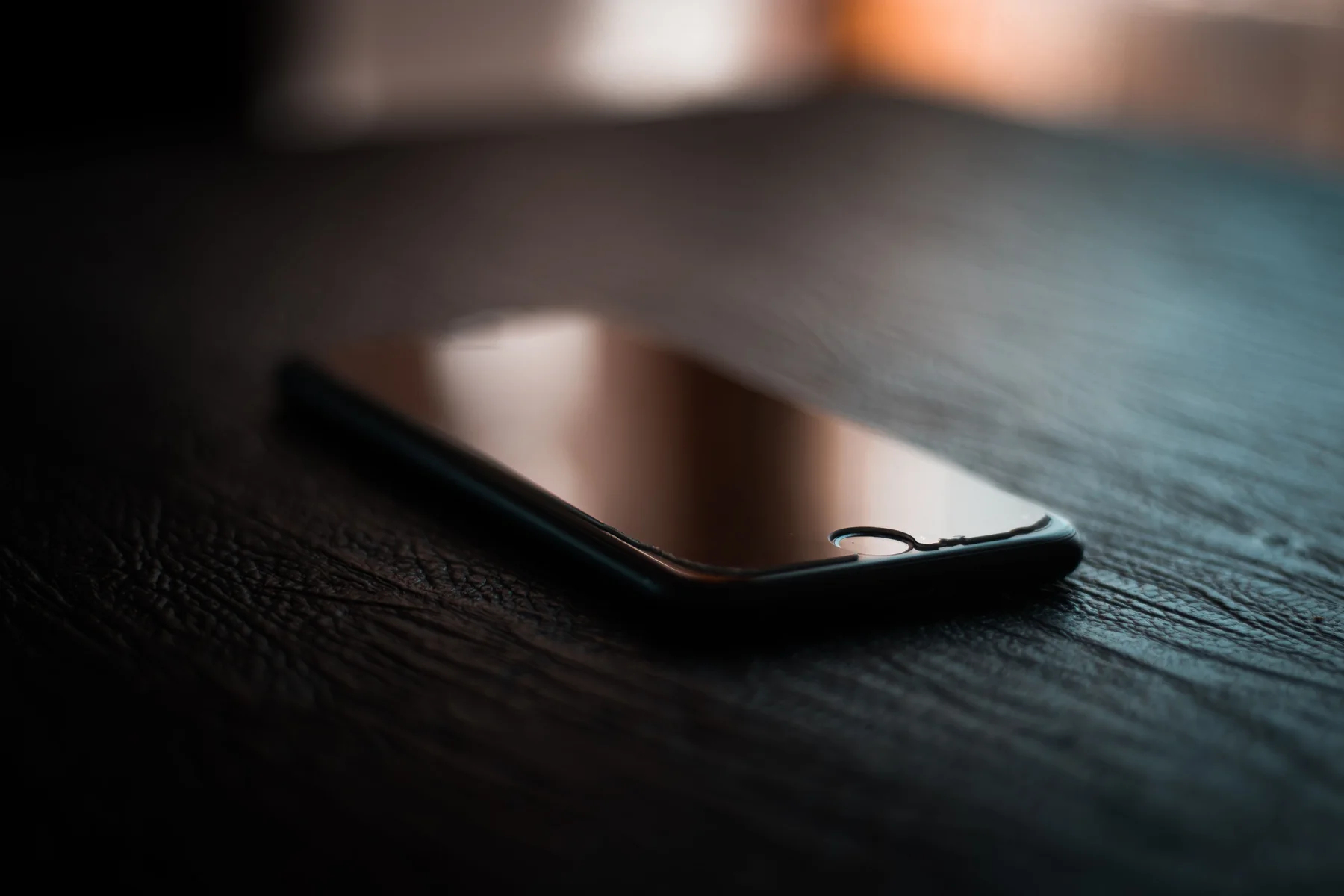 Ein Telefon mit dem Display nach unten auf einem dunklen Holztisch.