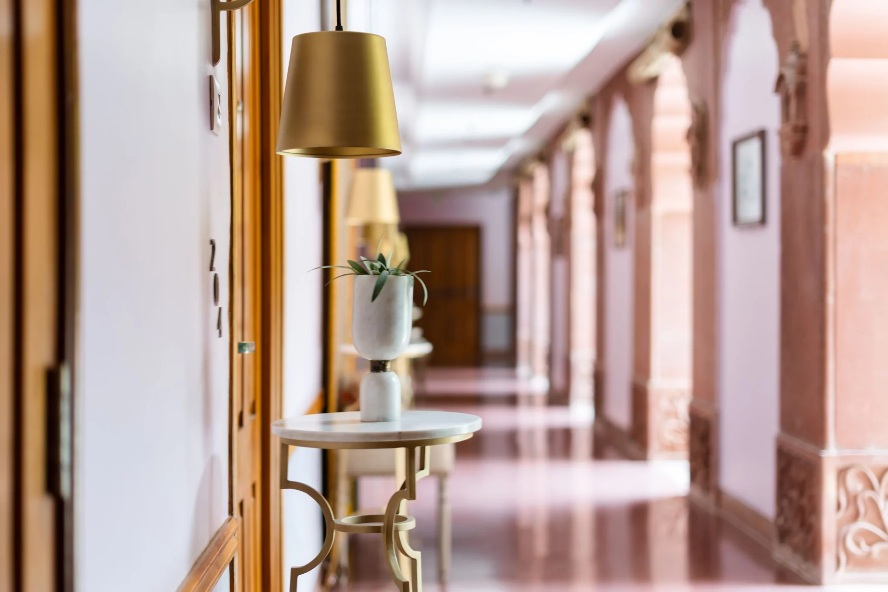 Ein Hotelflur mit Rundbögen, warmem Licht und einem kleinen Beistelltisch.