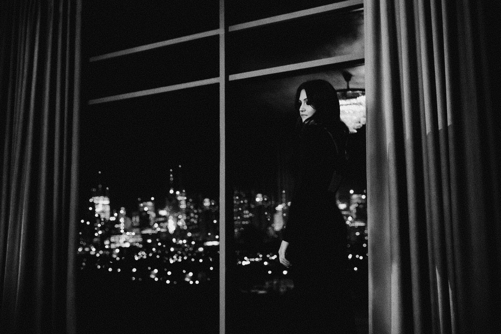 Abendlicher Blick durch eine Fensterfront auf die Lichter einer Stadt.