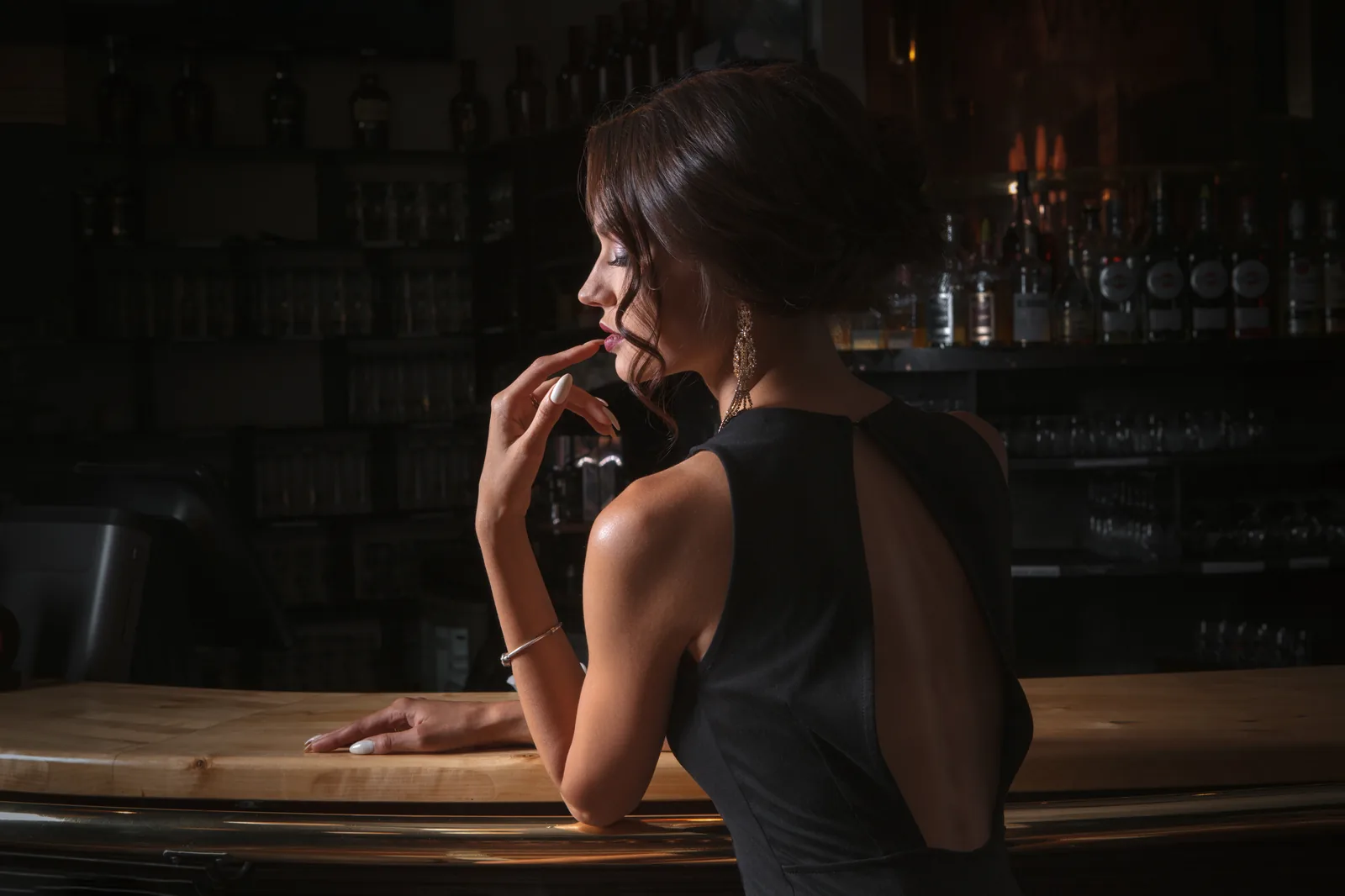 Eine Frau sitzt allein an einer Bar, im Hintergrund Flaschenregale.
