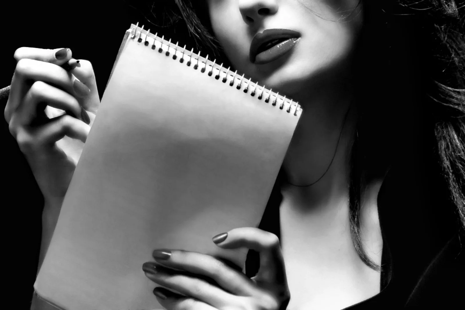Eine Frau hält einen aufgeschlagenen Notizblock und einen Stift.